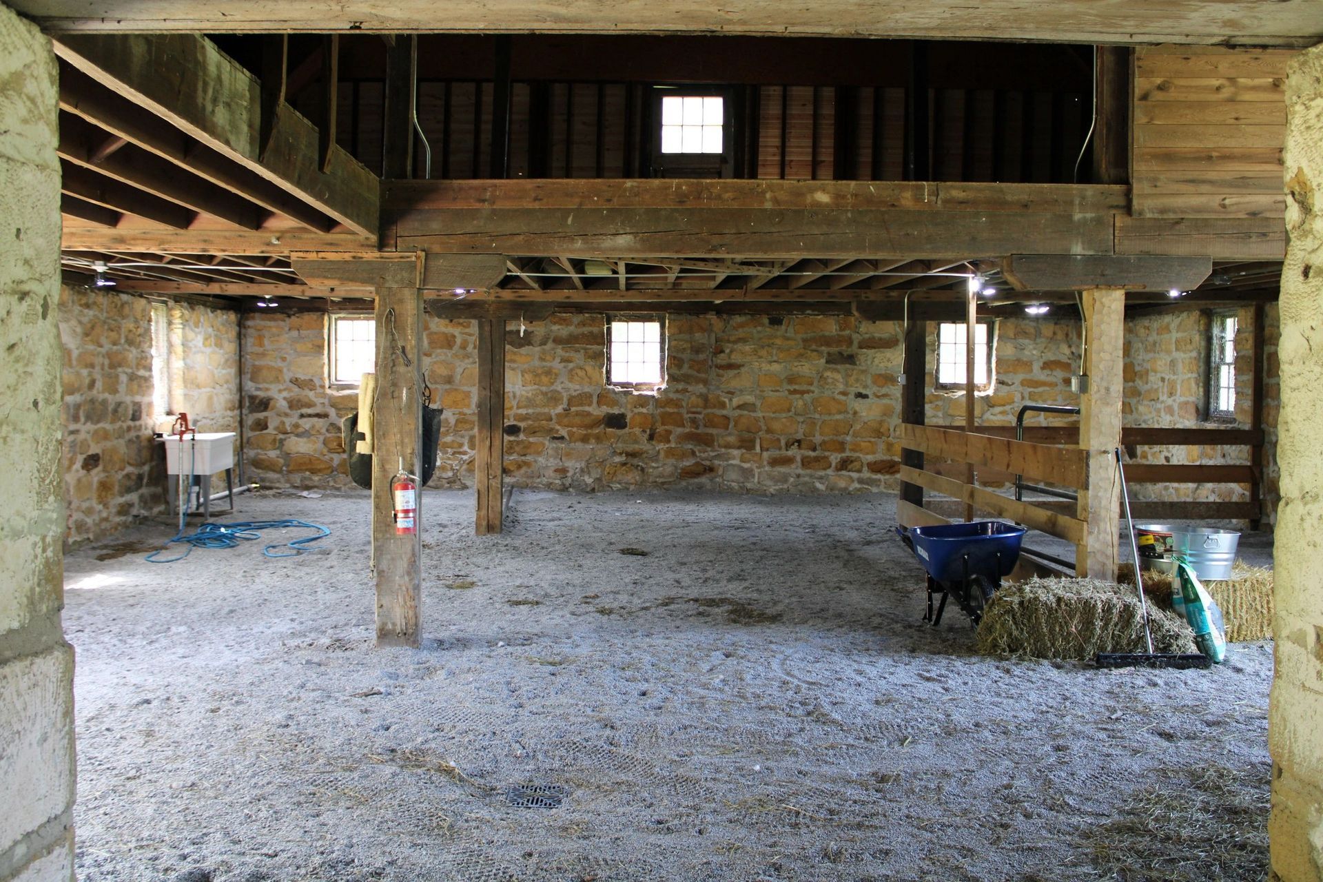 Interior of a stone barn with a gravel floor, wooden beams, and a hay bale.
