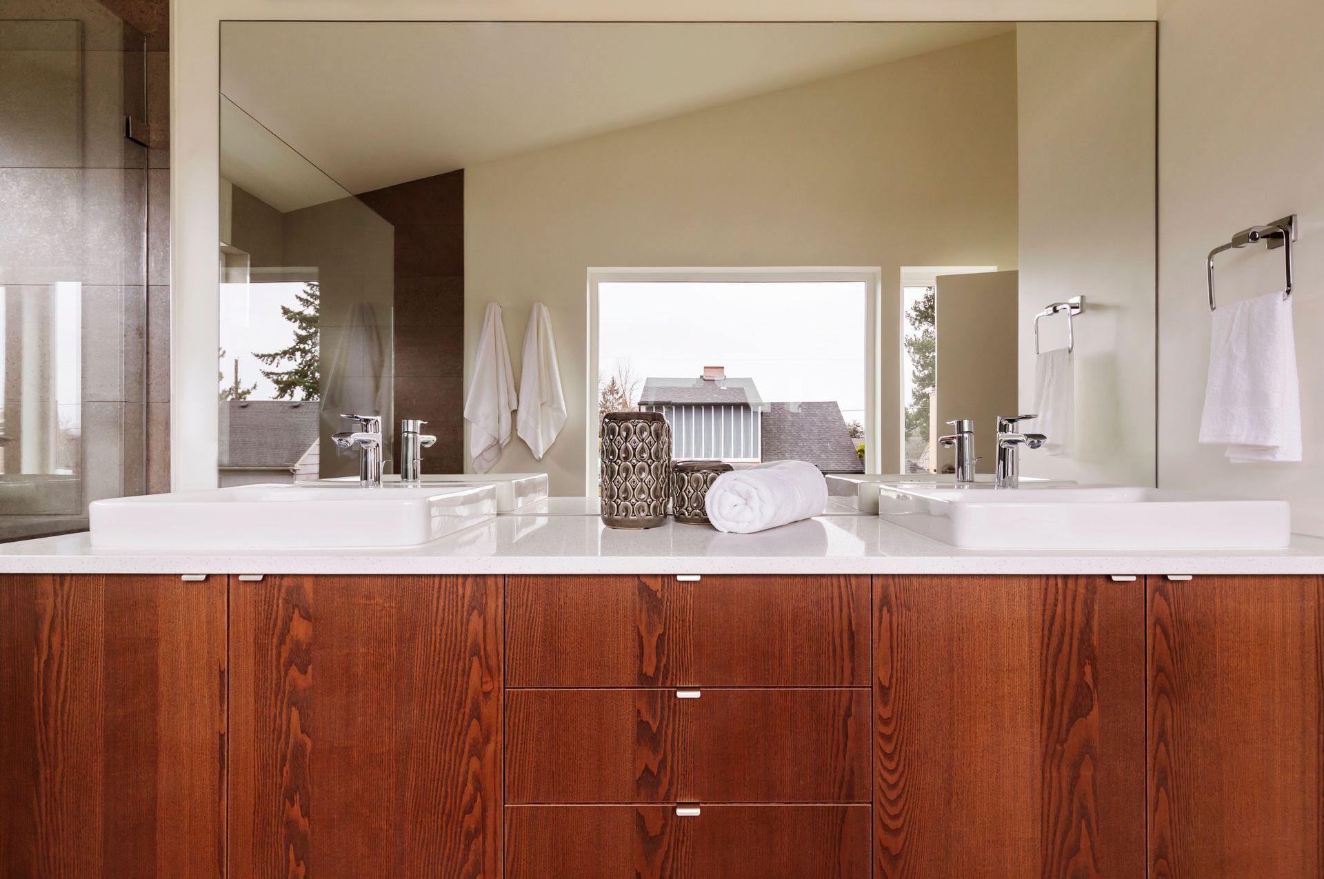 Bathroom with double sinks, large mirror, and wood vanity. White towels and a scenic window view.