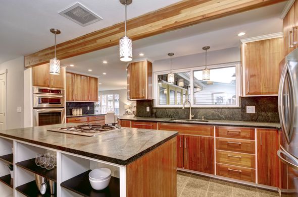 Modern kitchen with wooden cabinets, island with stovetop, granite countertops, and pendant lights.