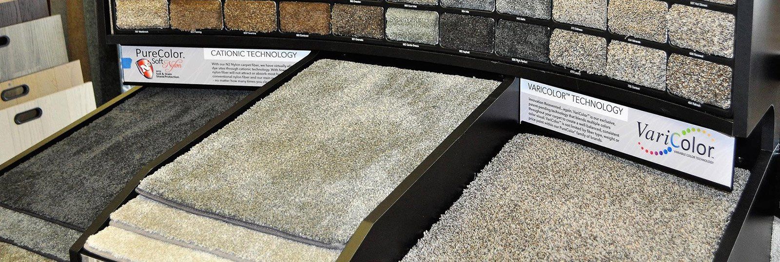 Carpet samples on display in a store, various neutral colors and textures.