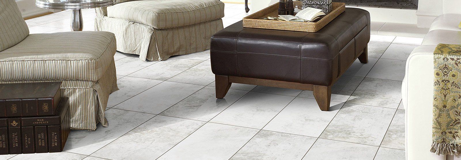 Living room with white plank flooring, brown leather ottoman, beige upholstered furniture.