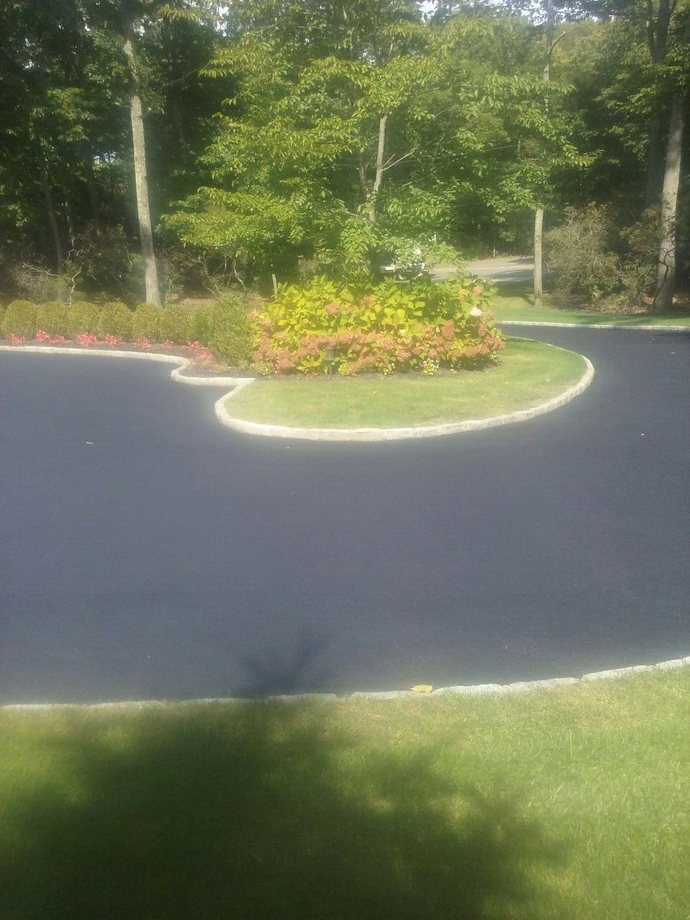 A black asphalt driveway surrounded by grass and trees.