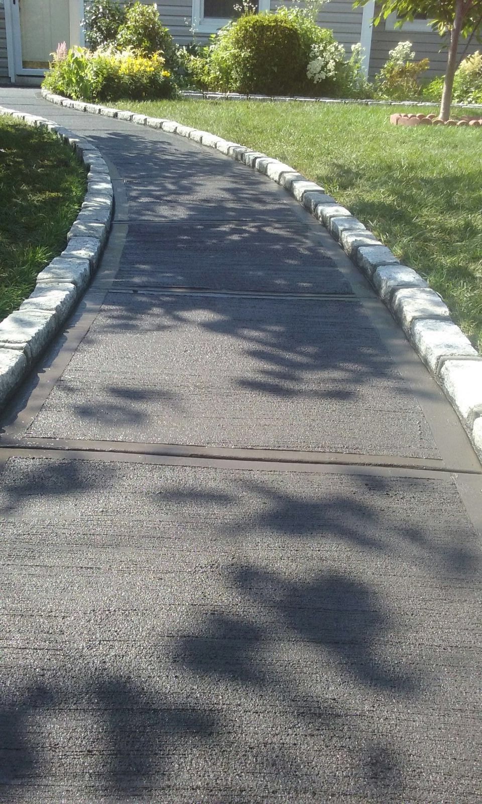 A concrete walkway leading to a house with a stone curb.