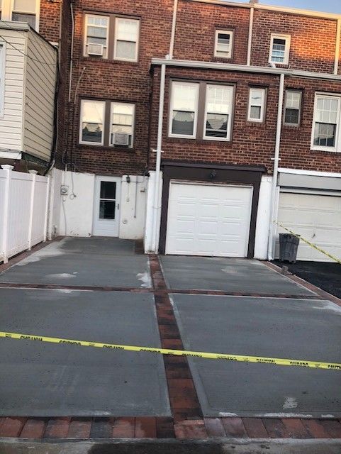 A brick building with a white garage door is behind a concrete driveway.