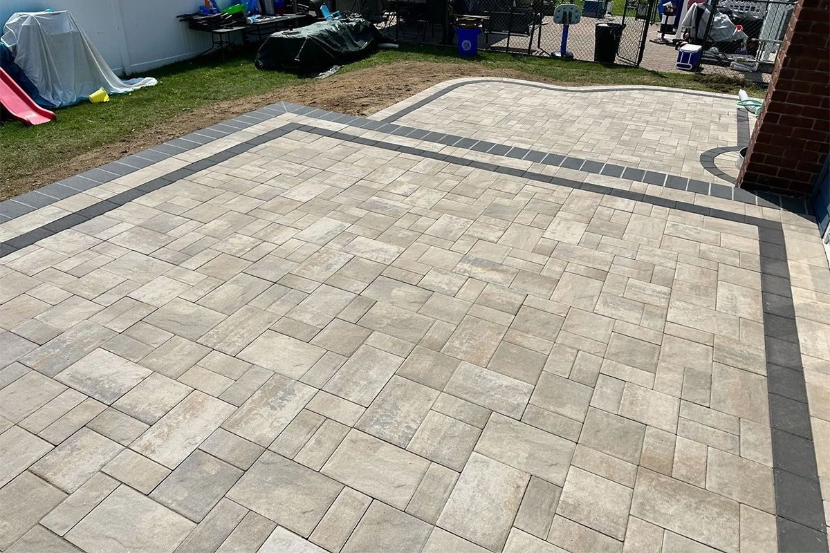 A brick patio with a black border in a backyard.