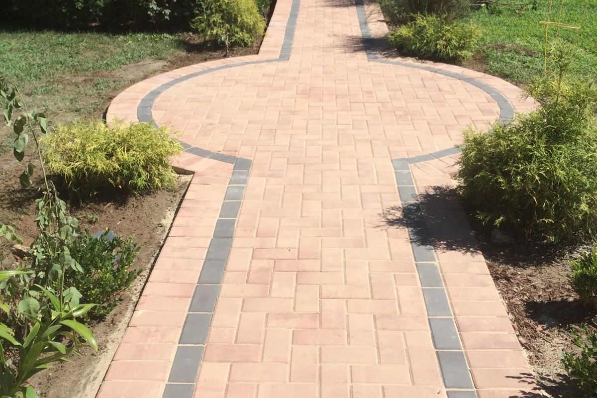 A brick walkway in a garden with a circle in the middle.