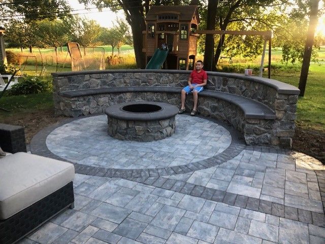 A boy sits on a stone bench next to a fire pit