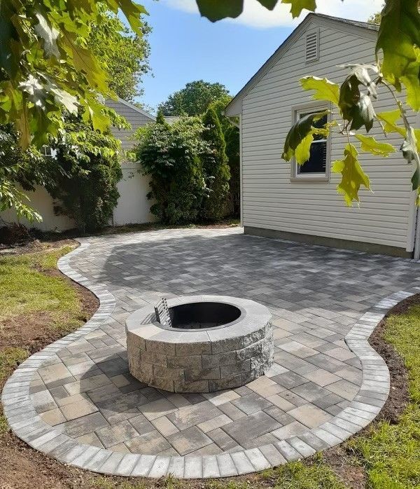 A fire pit in the middle of a patio in front of a house