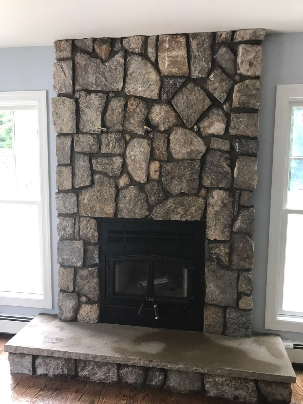 A living room with a stone fireplace and a window.
