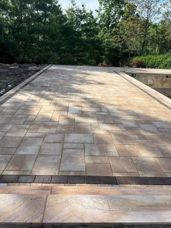 A brick driveway leading to a pool with trees in the background.