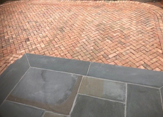 A brick patio with a blue stone border and a herringbone pattern.