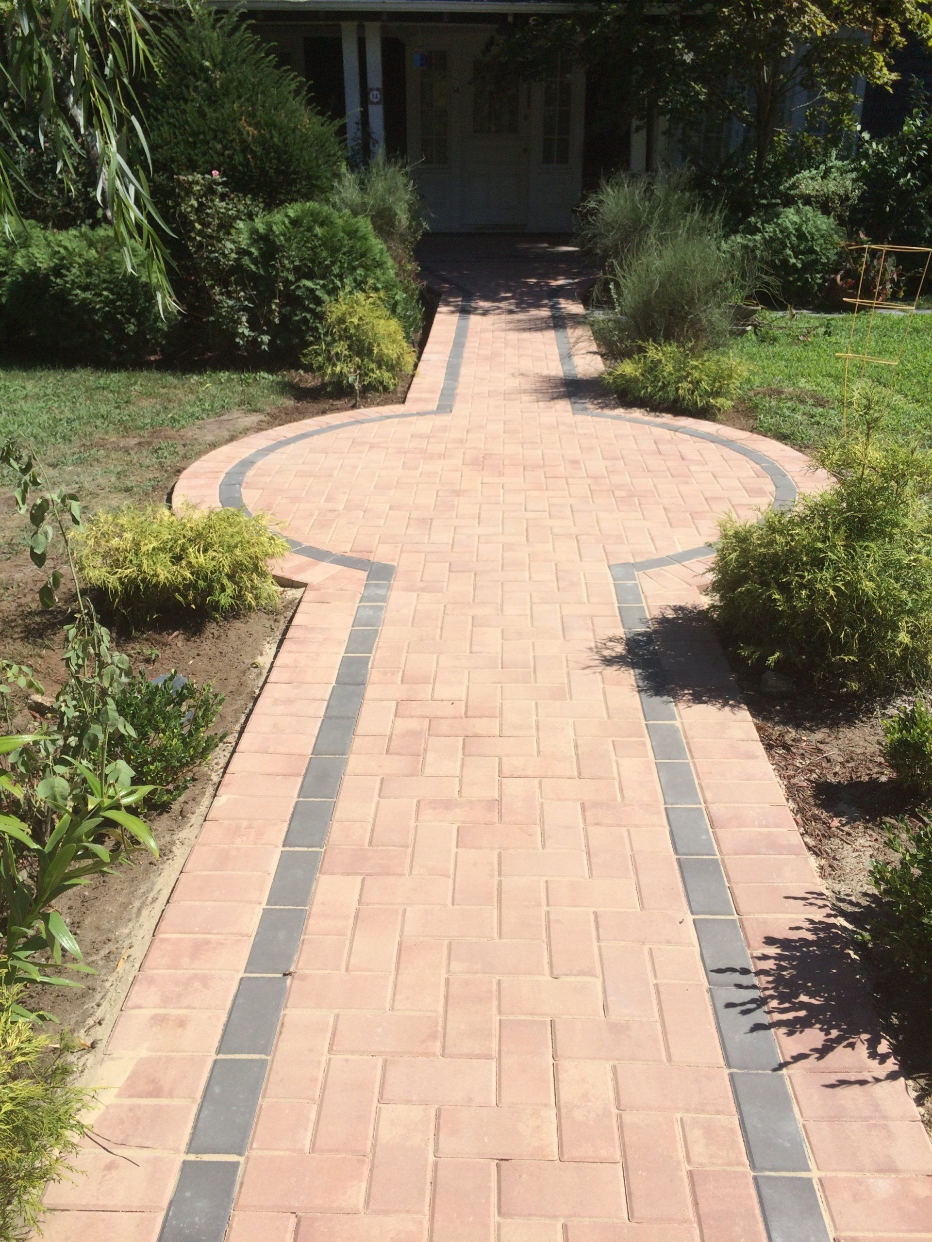 a brick walkway with bushes and grass
