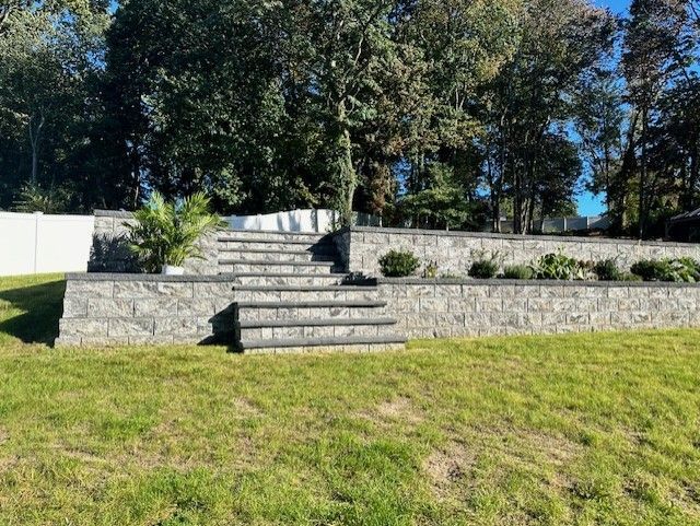 A stone wall with stairs leading up to it in a grassy yard.