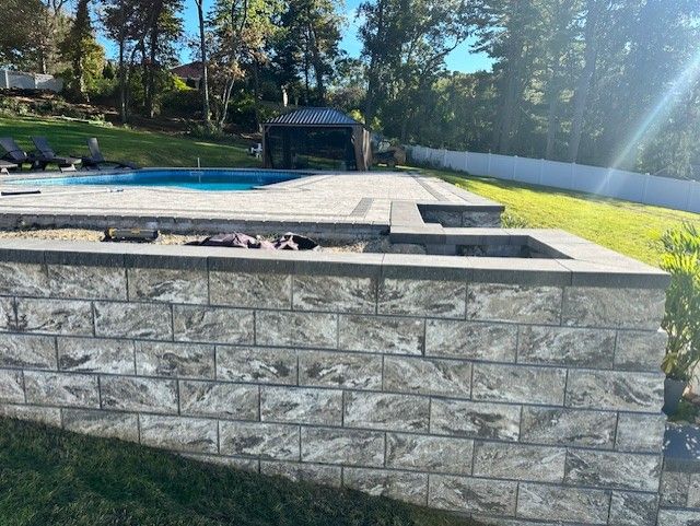A brick wall surrounds a swimming pool in a backyard.