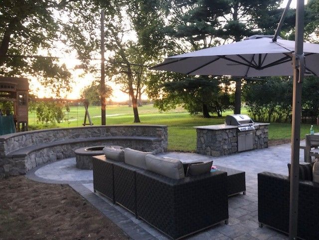 A patio with a couch , chairs , umbrellas and a grill