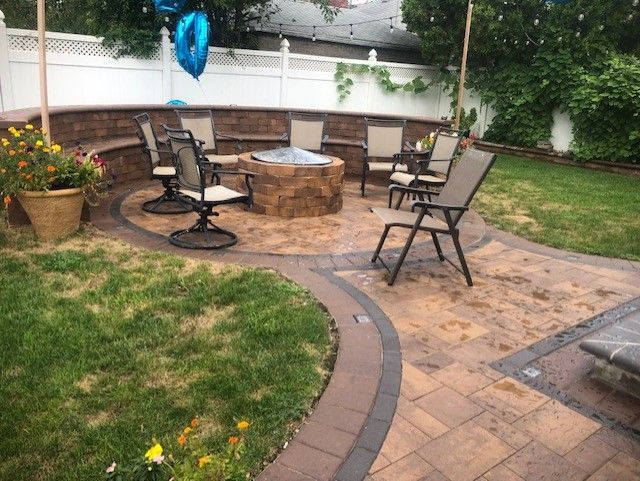 A patio with a fire pit and chairs in a backyard.