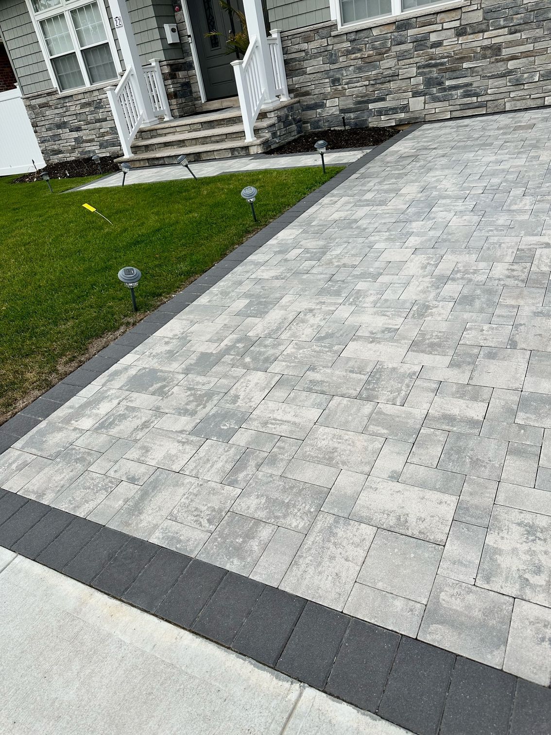 A brick driveway with a black border is in front of a house.