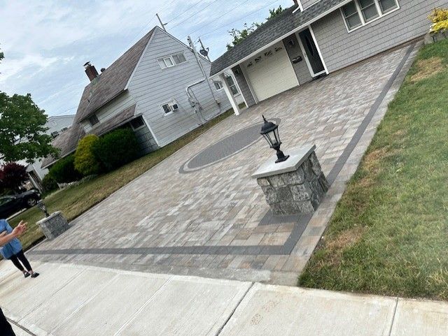 A brick driveway with a lamp post in front of a house.