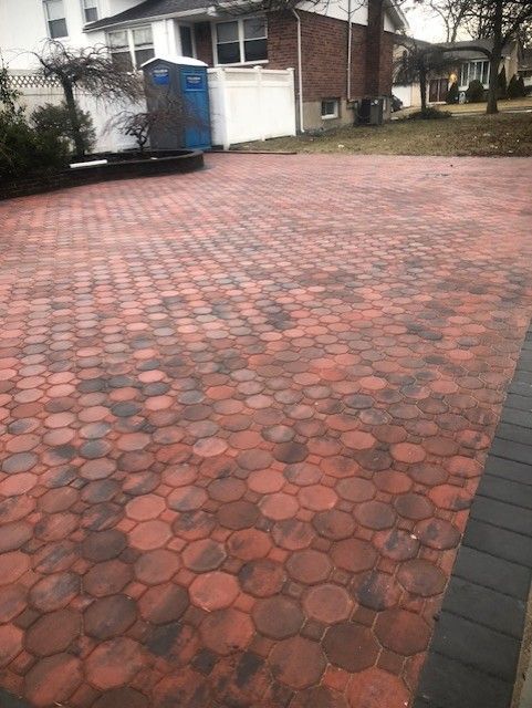 A brick driveway in front of a house with a blue portable toilet in the background.