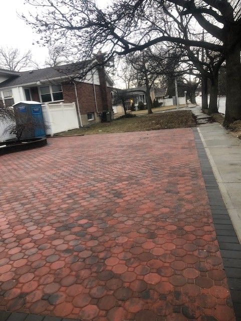 A brick driveway leading to a house with trees in the background.