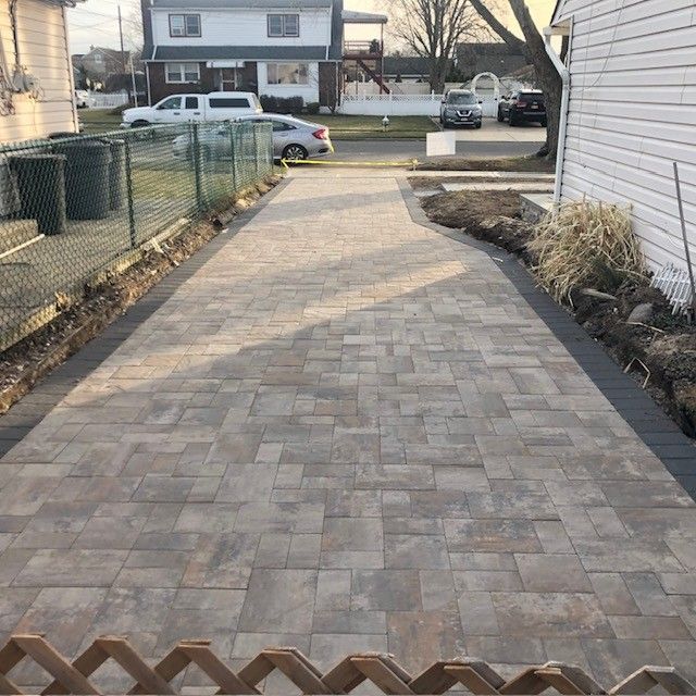 A brick driveway leading to a house with cars parked on the side of it.