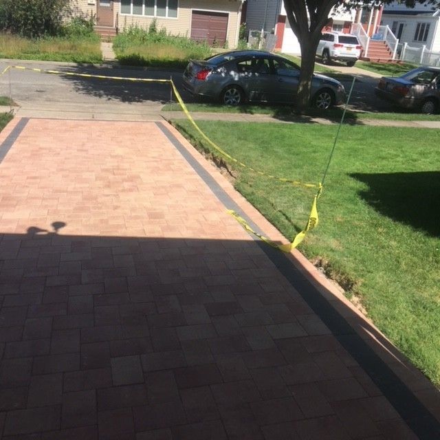 A car is parked on the side of a brick driveway