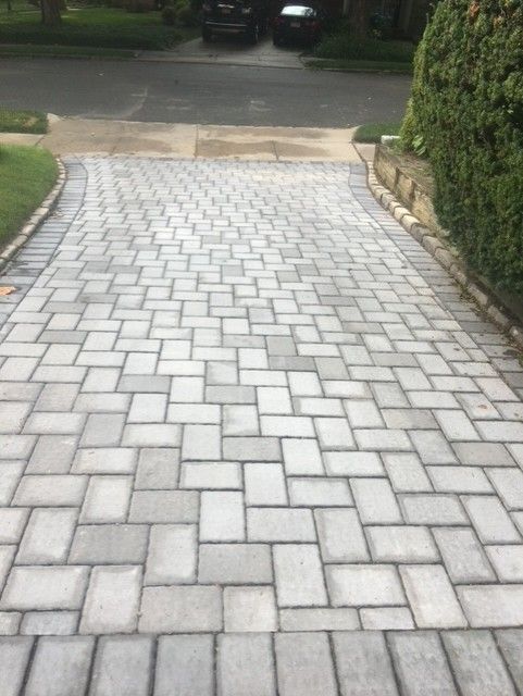 A brick driveway leading to a car parked on the side of the road.