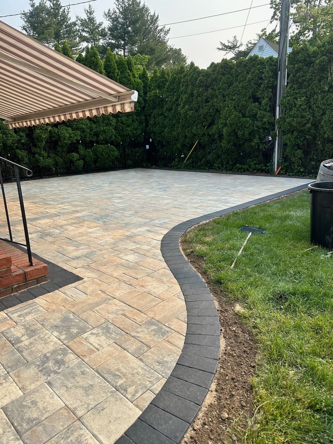 A patio with a canopy and a brick walkway in a backyard.