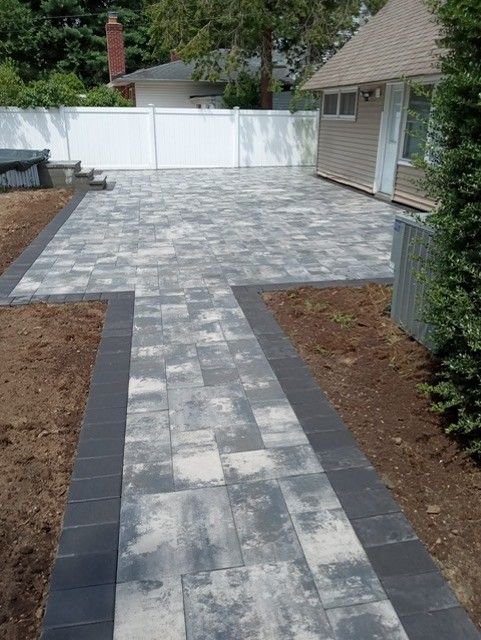 A brick walkway leading to a house with a white fence.