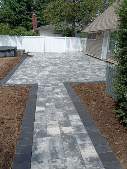 A brick walkway leading to a house with a white fence.