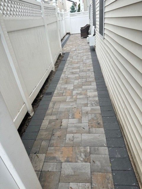 A brick walkway between two houses with a white fence.