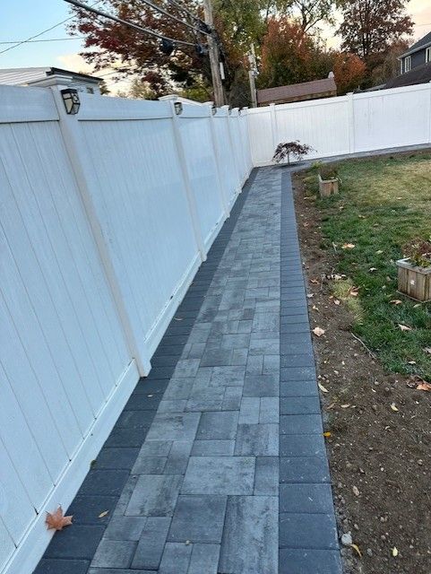 A dog is standing on a sidewalk next to a white fence.