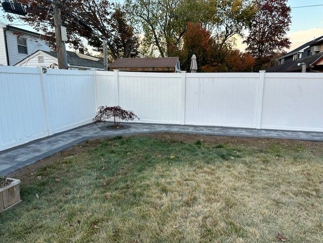 A white fence surrounds a lush green lawn in a backyard.