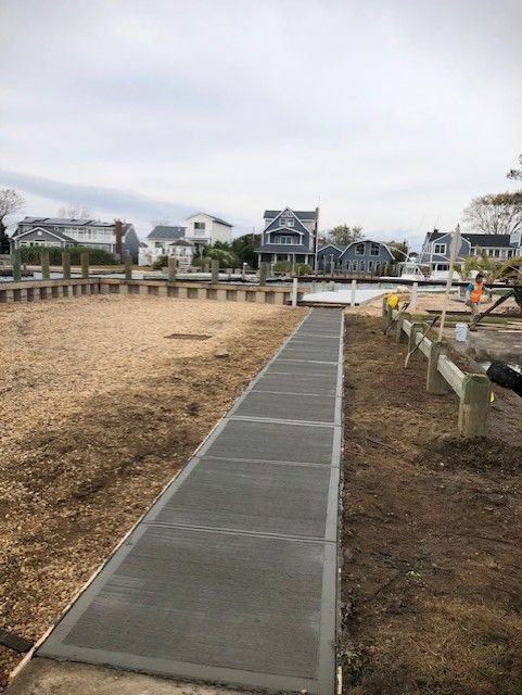 A concrete walkway leading to a dock with houses in the background.