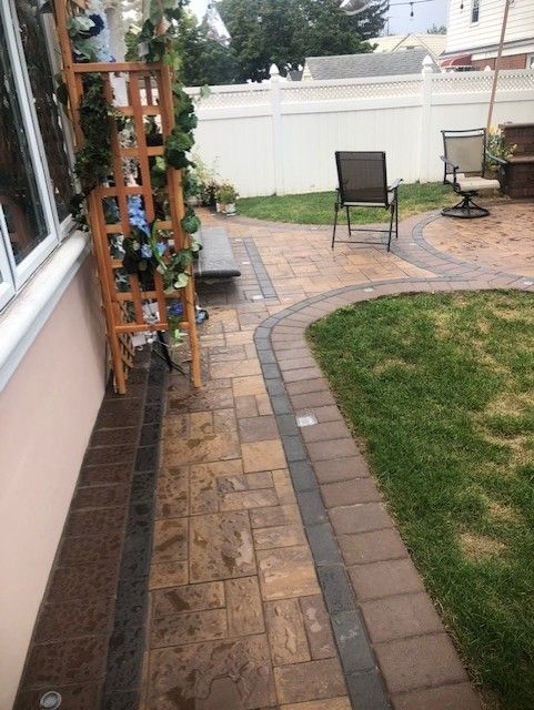 A brick walkway leading to a patio with chairs and a fence.