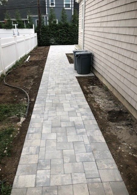 A brick walkway leading to a house with a white fence.