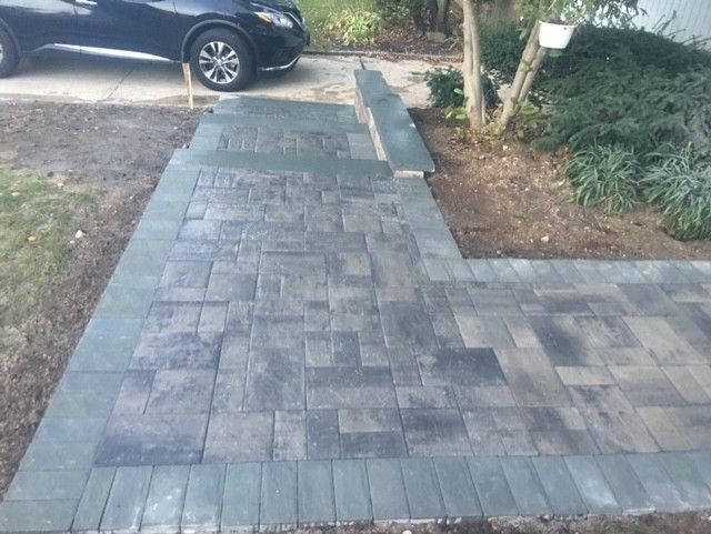 A black car is parked in a driveway next to a brick walkway.