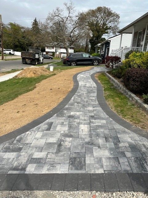 A brick walkway leading to a house with a truck parked on the side of the road.