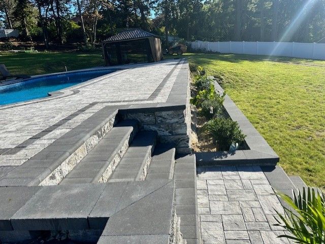 A patio with stairs and a pool in the background.