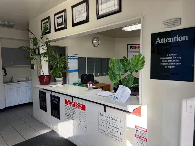 Reception desk in a clinic lobby with plants, framed certificates, and an “Attention” sign.
