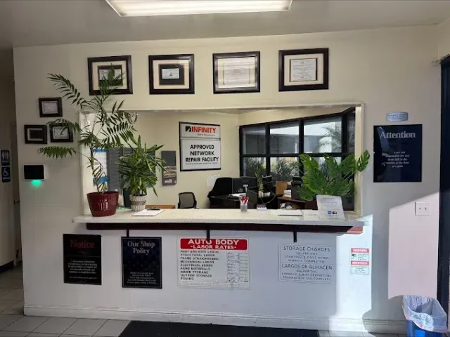 Reception desk with plants, framed signs, and a windowed office behind it