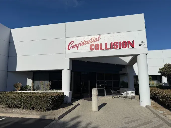 Collision repair shop exterior with white facade and red signage under a blue sky