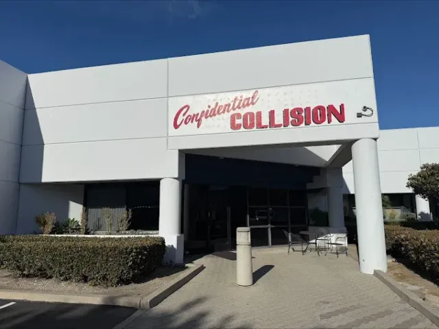 Front entrance of Collision repair shop with white facade and red signage under a clear blue sky