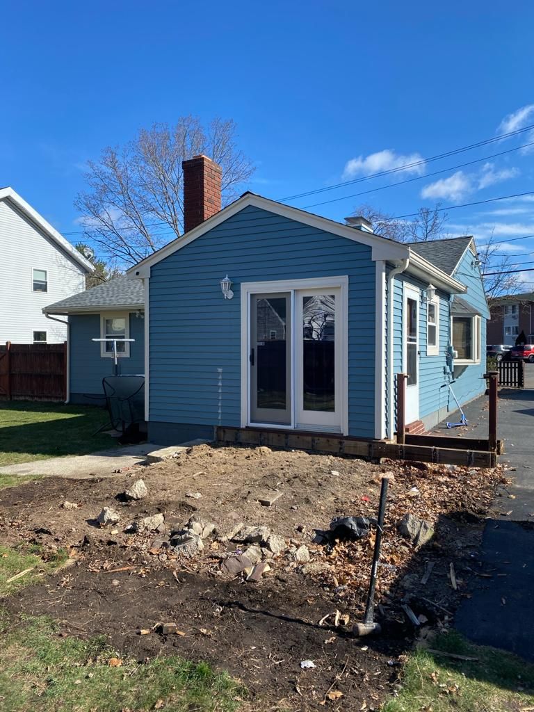 Blue house with sliding doors and a brick chimney overlooking a yard area under construction with loose dirt and rocks.
