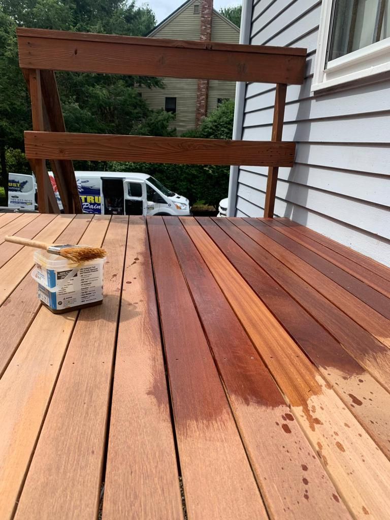 A wooden deck in the process of being stained, showing a contrast between the raw, light boards and the deep-toned finish.