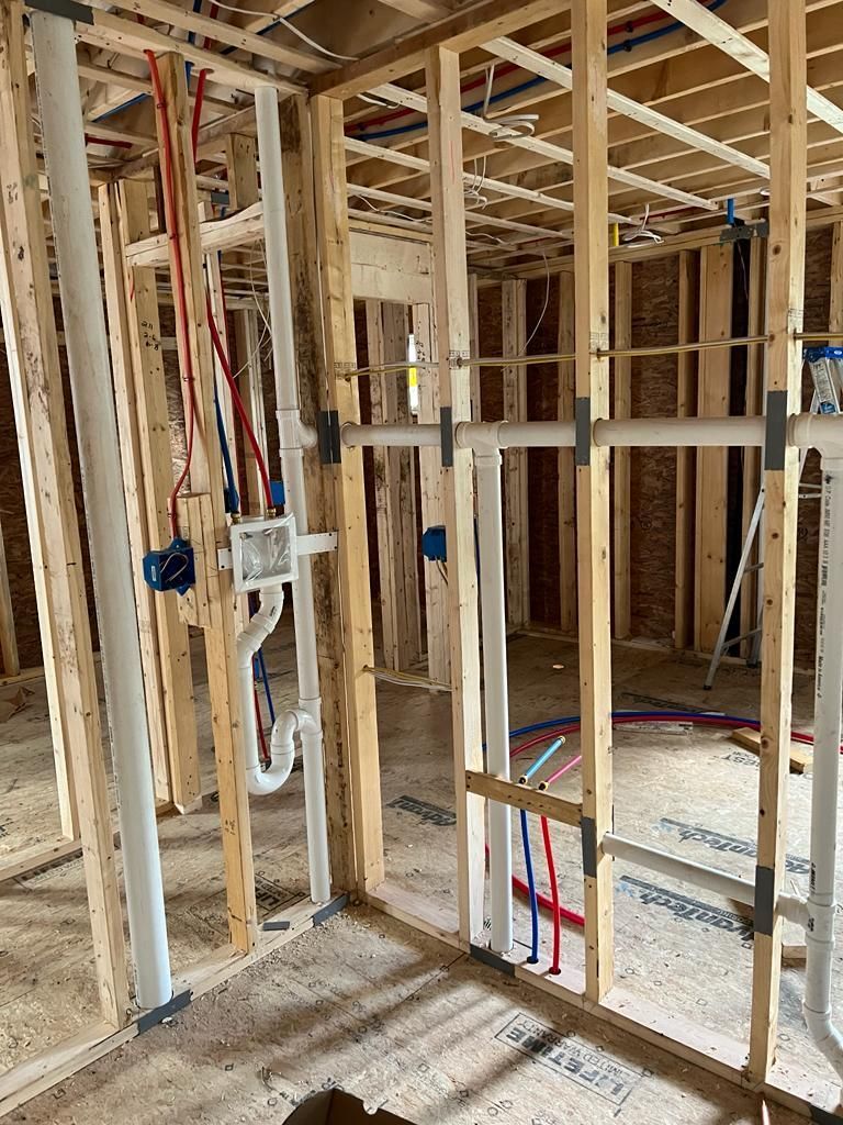 Unfinished interior framing of a building showing wall studs, plumbing pipes, and electrical boxes in a wooden structure.