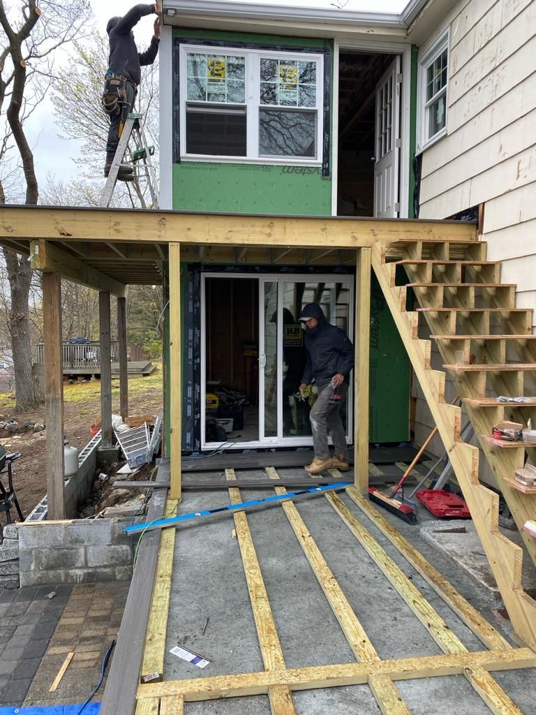 Construction workers building a deck and stairs outside a house, with a sliding glass door installed on the lower level.