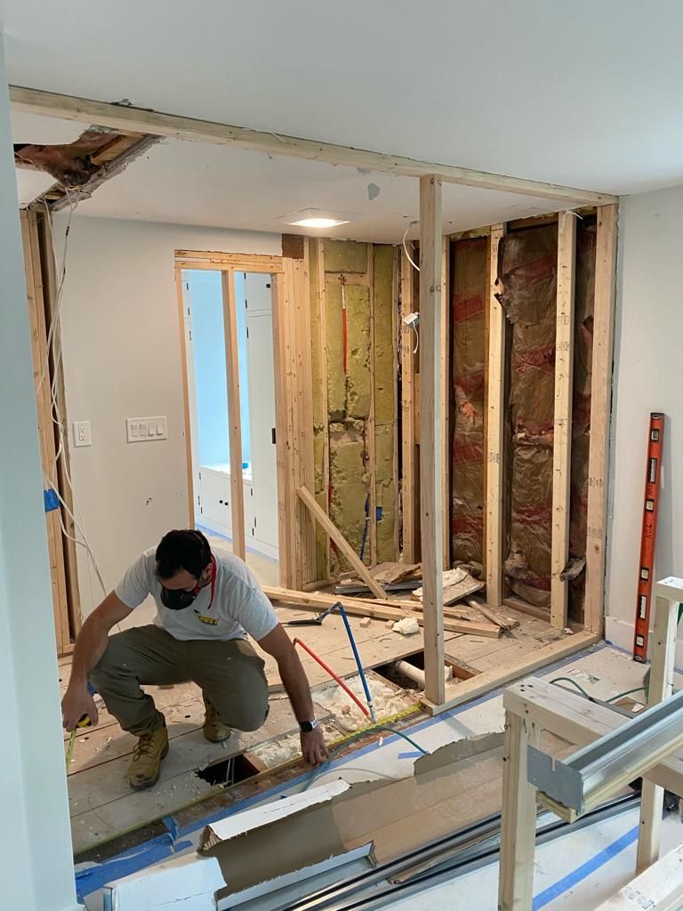 A person works on a wooden wall frame in a room undergoing interior construction.