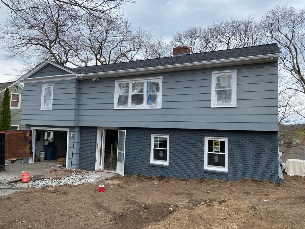A two-story house under renovation with light gray siding on the top, dark gray shingles on the bottom, and new windows.