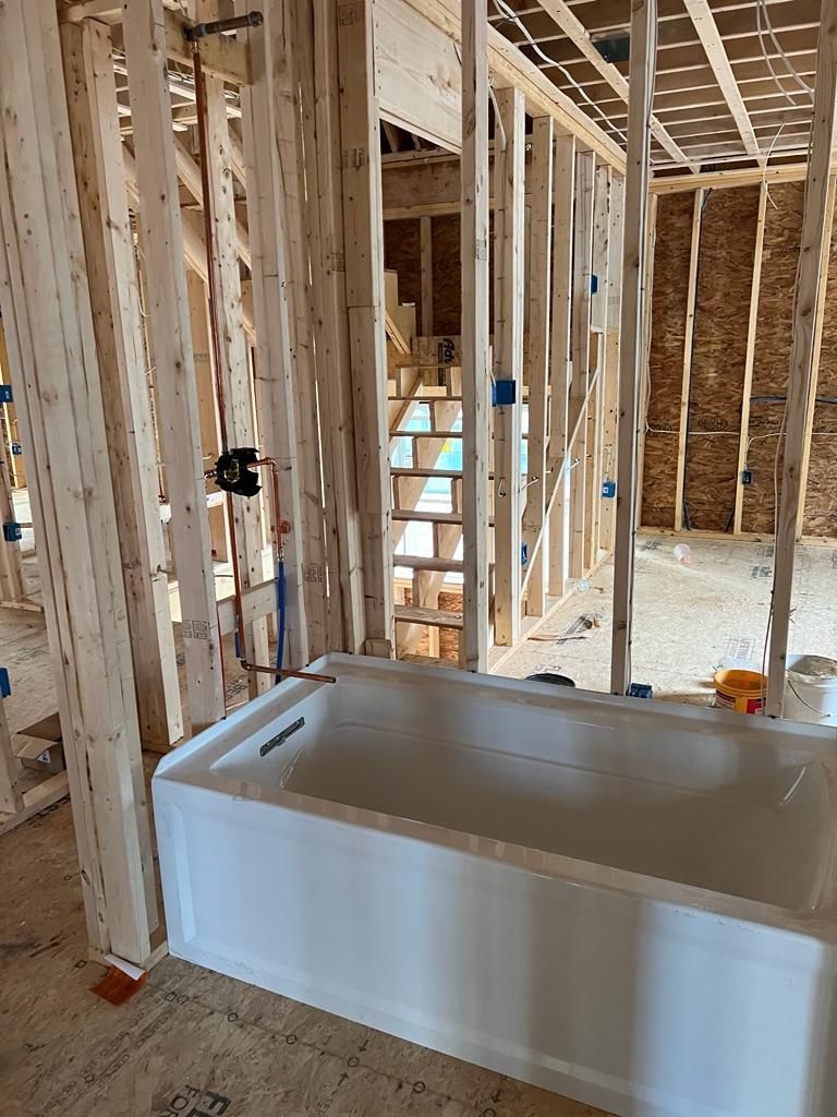 A new white bathtub installed in a framed-out room during construction, showing exposed wall studs and plumbing pipes.